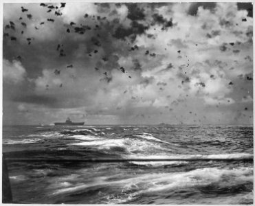 A Japanese bomb splashes astern of a U.S. carrier as the enemy plane pulls out of its dive above the carrier. In the... - NARA - 520596