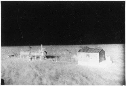 (Operation Cue) - One-story shed beside LP (liquified petroleum) tank - both smoldering from heat of flash - NARA - 541790