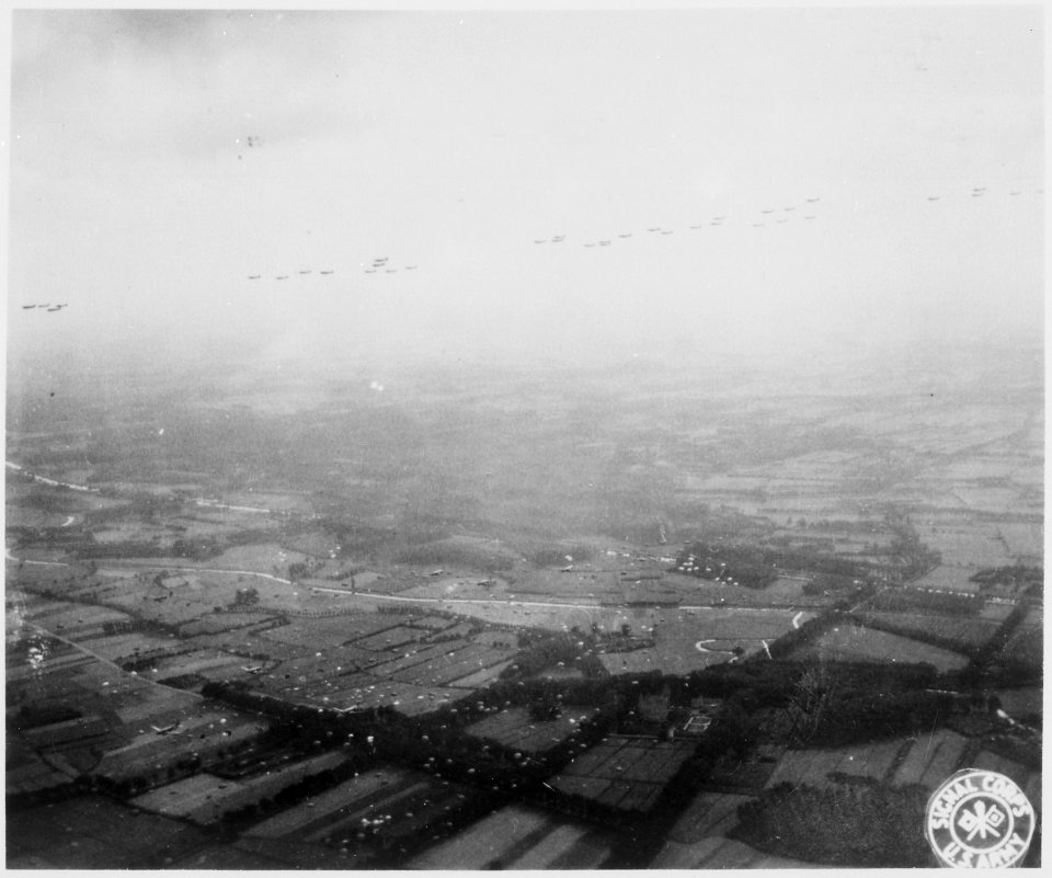 A fleet of Allied aircraft flies overhead as paratroopers of the Allied Airborne Command float groundward in the... - NARA - 531308