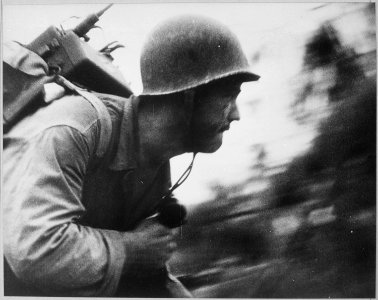 A US Marine charges across the beach on Peleliu Island, Palau Islands, the walkie talkie firmly strapped to his... - NARA - 520617