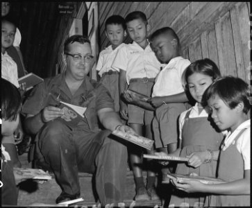 A U.S. Air Force airman distributes books to Thai children at Korat, Thailand. - NARA - 542307 photo