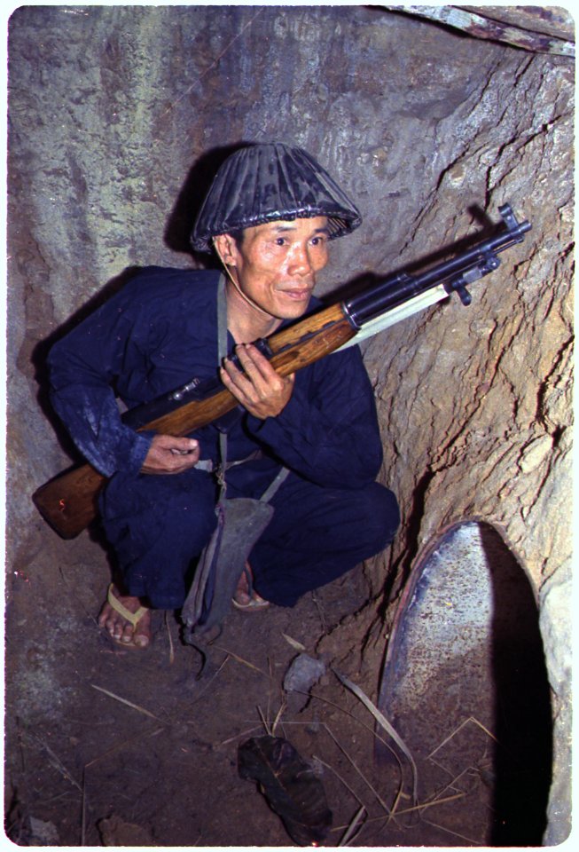 A Viet Cong soldier crouches in a bunker with an SKS rifle. - NARA - 530624