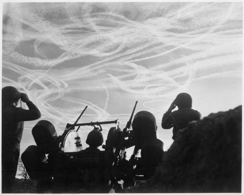 Alerted GIs of M-51 Anti-aircraft Battery are silhouetted against German sky streaked with vapor trails from allied... - NARA - 531232