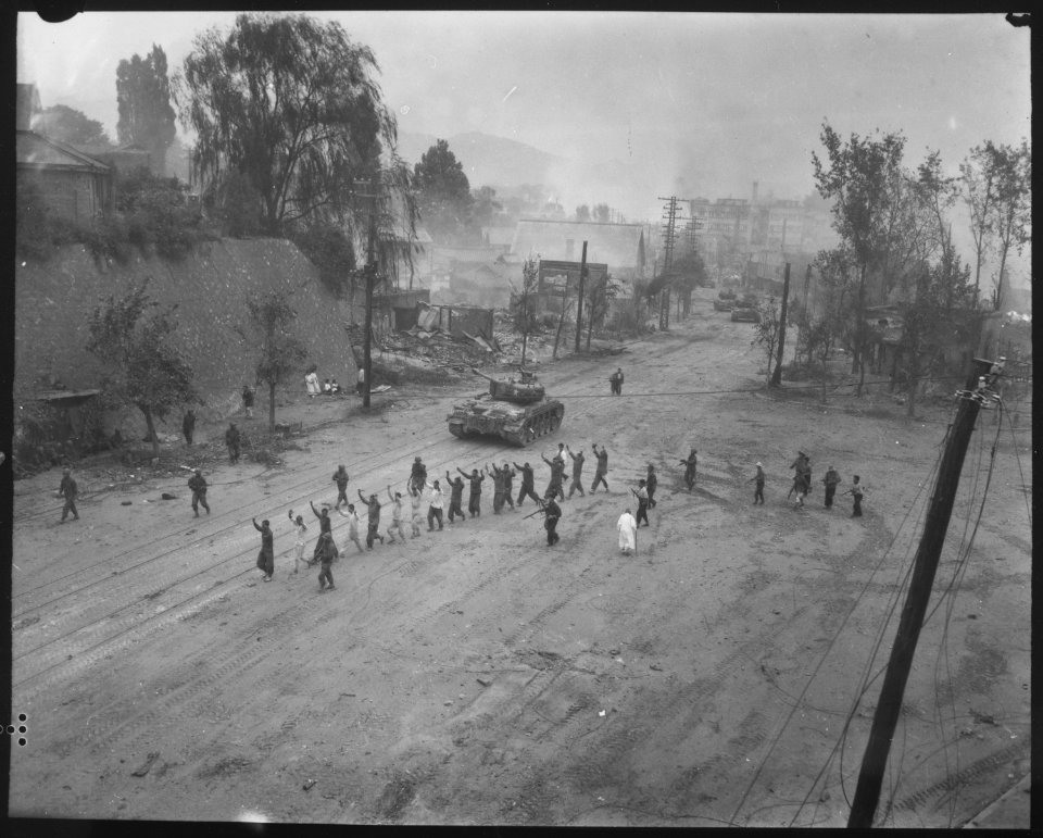 A U.S. Marine tank follows a line of prisoners of war down a village street. - NARA - 532408