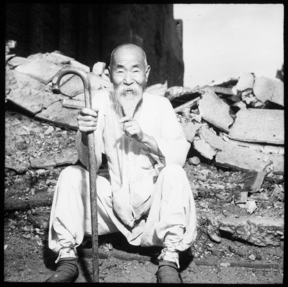 An old Korean man takes a rest on the street in front of destroyed buildings, in Seoul. - NARA - 530637