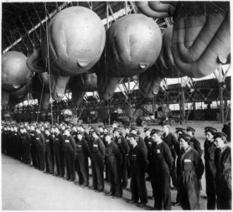 Balloons safely tucked away in the hangar for the night. W.A.A.F. balloon operators report for inspection before... - NARA - 541911