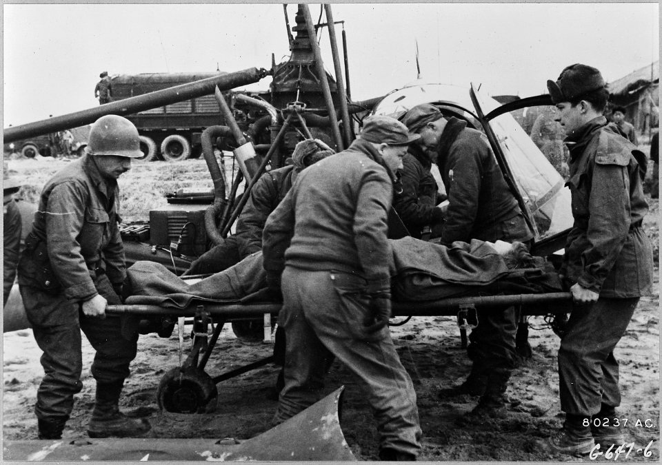 Corporal Eader (center with back to camera) reassures a wounded soldier as medics carry him away from Captain... - NARA - 542227