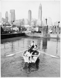 Four young members of the Madison Square Boy's Club rowing a boat in a rooftop pool, Manhattan skyscrapers in the backgr - NARA - 541907