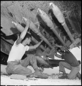 Five-inch rockets being loaded under the wing of an F4U of MAG-33. Just before take-offs, the safety pins are removed... - NARA - 532561