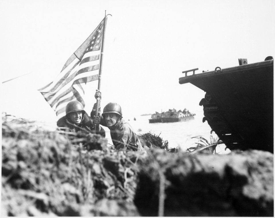 First flag on Guam on boat hook mast. Two U.S. officers plant the American flag on Guam eight minutes after U.S.... - NARA - 532532