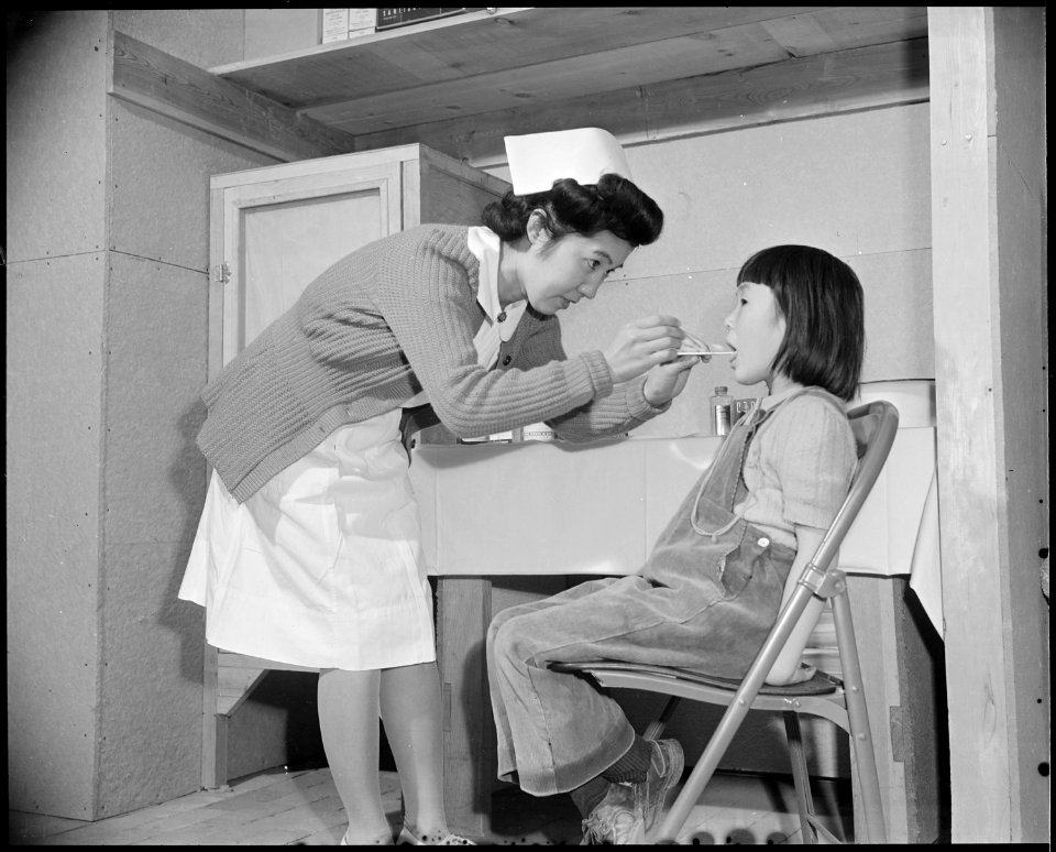 Granada Relocation Center, Amache, Colorado. The school nurse administers a throat swabbing to a yo . . . - NARA - 539056