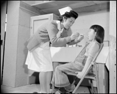 Granada Relocation Center, Amache, Colorado. The school nurse administers a throat swabbing to a yo . . . - NARA - 539052
