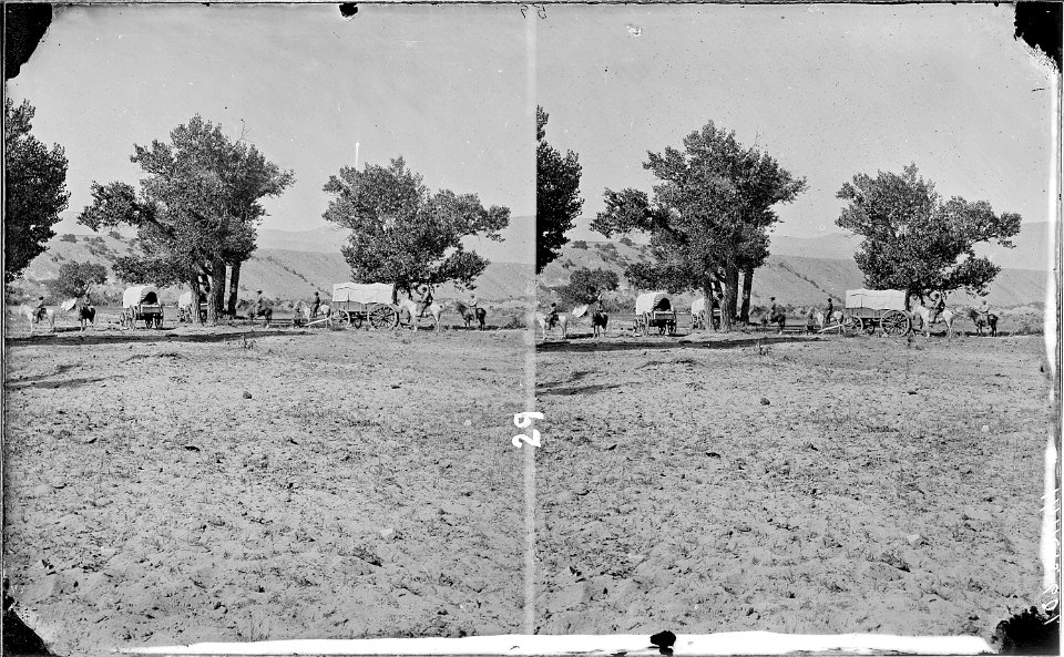 Harrell's Camp. Brown's Park, Wyoming, 1871. 3 covered wagons, 5 men mounted on horses (horse extreme left of photo... - NARA - 517870