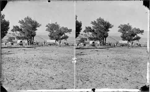 Harrell's Camp. Brown's Park, Wyoming, 1871. 3 covered wagons, 5 men mounted on horses (horse extreme left of photo... - NARA - 517870