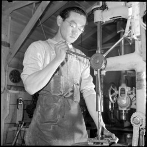 Heart Mountain Relocation Center, Heart Mountain, Wyoming. A young machinist operates a drill press . . . - NARA - 539258