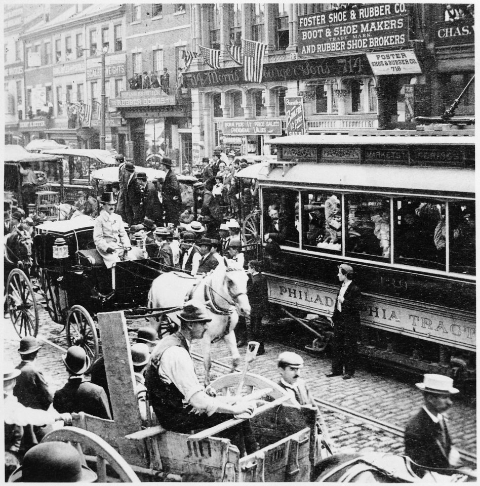 Horse-drawn wagons and carriages, an electric trolley car, and pedestrians congest a cobblestone Philadelphia street in - NARA - 513362