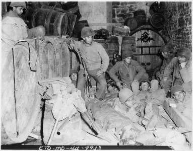 Infantrymen take a short rest before pushing on, in a deserted house in the French town of Tessy sur Vire. Our... - NARA - 531200