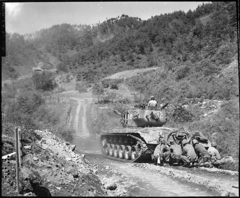 Marine infantrymen take cover behind a tank while it fires on Communist troops ahead. Hongchon Area, May 22, 1951. - NARA - 532415