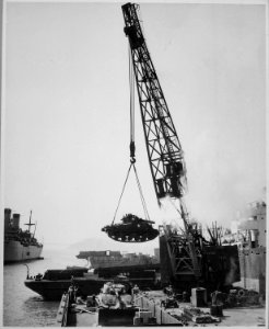 Marine Corps tanks-ready for the front lines-are swung aboard a barge at the Naval Supply Center by crane, for... - NARA - 541949