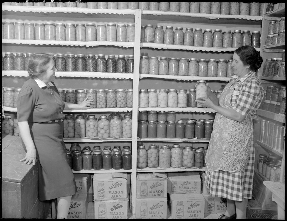 New Mexico. Mrs. Fidel Romero proudly exhibits her canned food.. (Two women standing in a kitchen pantry. Pantry... - NARA - 513405