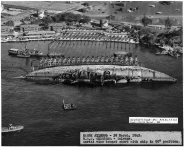NASPH ^118506- 19 March 1943. USS Oklahoma- Salvage. Aerial viwe toward shore with ship in 90 degree position. - NARA - 296975