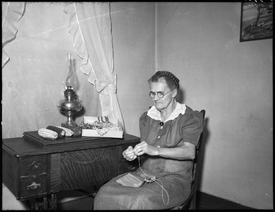 No original caption. (Elderly woman sitting at a small table sewing.) - NARA - 513402