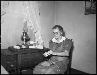 No original caption. (Elderly woman sitting at a small table sewing.) - NARA - 513402 photo