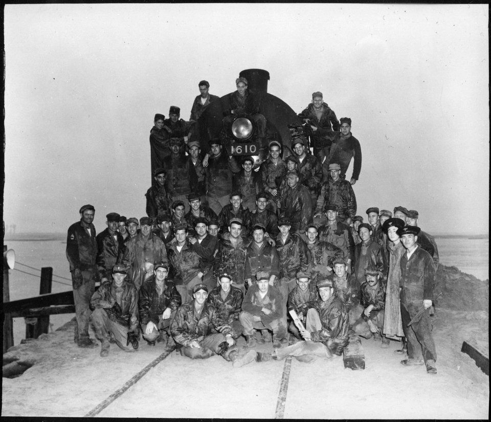 Officers and men of the 62nd Engineers stand in front of the first train to cross the new railroad bridge which they... - NARA - 531382