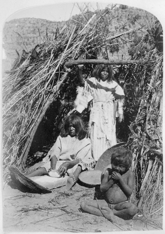 Paiute woman grinding seeds in doorway of thatched hut, small boy in foreground, 1872 - NARA - 517728