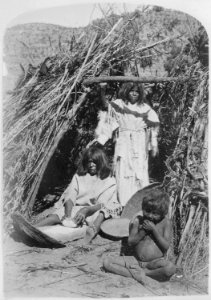 Paiute woman grinding seeds in doorway of thatched hut, small boy in foreground, 1872 - NARA - 517728