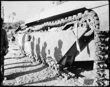 On the flank of a battle-wrecked alligator tank the Okinawa sun casts the shadows of 6th Division Marines as they... - NARA - 532563