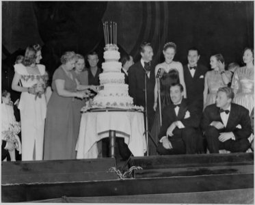 Photograph of First Lady Bess Truman cutting the cake at the Roosevelt Birthday Ball, as Paul Henreid, Alexis Smith... - NARA - 199257