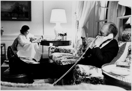 Photograph of First Lady Betty Ford Reading a Newspaper, while President Ford Talks on the Telephone, in the Second... - NARA - 186793