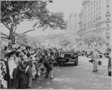 Photograph of General Dwight D. Eisenhower standing up in the back of his jeep, saluting flag-waving crowds along a... - NARA - 199112