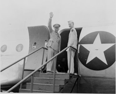 Photograph of General Dwight D. Eisenhower waving to a crowd as he prepares to board an Army airplane, flanked by his... - NARA - 199124