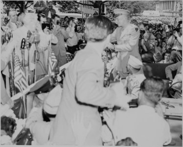 Photograph of General Dwight D. Eisenhower standing in the back of his jeep, surrounded by photographers and cheering... - NARA - 199113