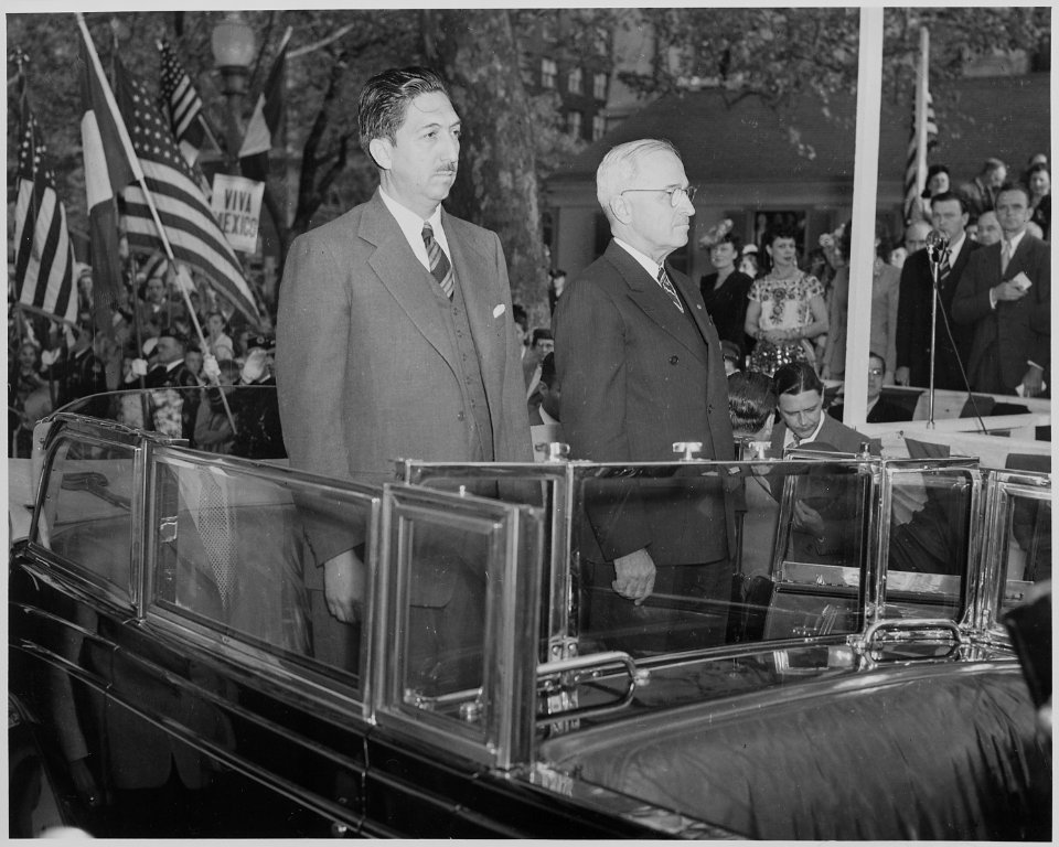 Photograph of Mexican President Miguel Aleman and President Truman standing in the back of an open limousine during... - NARA - 199562