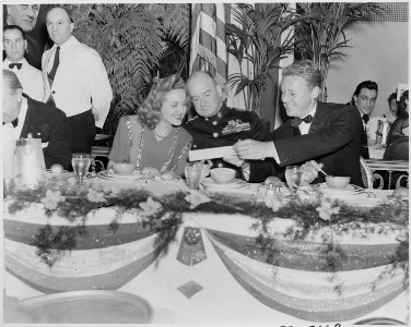 Photograph of movie stars Constance Moore and Van Johnson, seated at a table with an unidentified military officer... - NARA - 199324