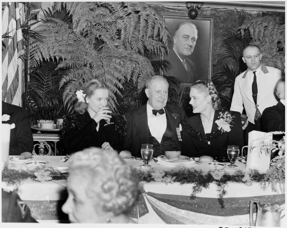 Photograph of movie stars Diana Lynn and Alexis Smith, seated at a table with an unidentified man during the... - NARA - 199326