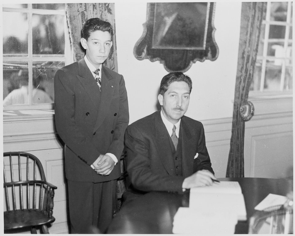 Photograph of President Miguel Aleman of Mexico signing the guest book at Mount Vernon, as an unidentified young man... - NARA - 199550