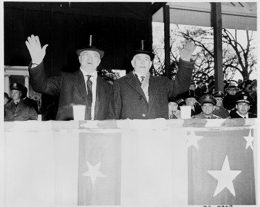 Photograph of President Truman and Vice President Barkley waving from the reviewing stand during the Inaugural parade. - NARA - 200065