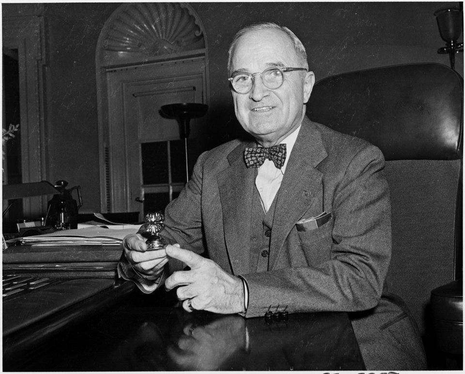 Photograph of President Truman at his desk in the Oval Office, holding a four-leaf-clover paperweight. - NARA - 200414