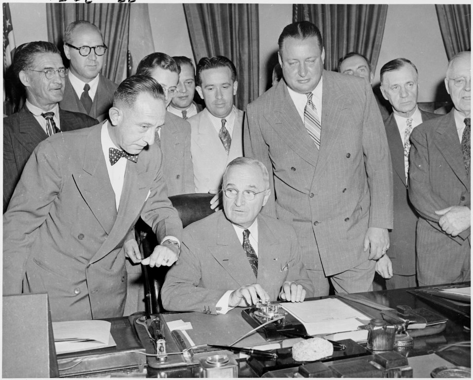Photograph of President Truman at his desk in the Oval Office, preparing to press a button activating a new generator... - NARA - 200115