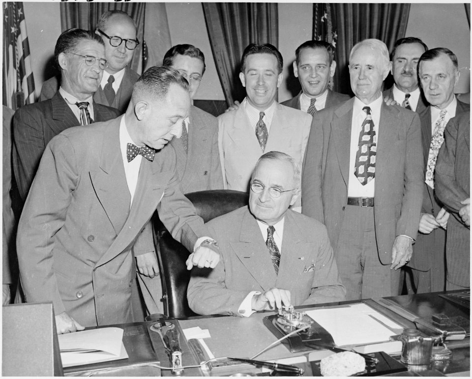 Photograph of President Truman at his desk in the Oval Office, preparing to push a button activating a new generator... - NARA - 200114