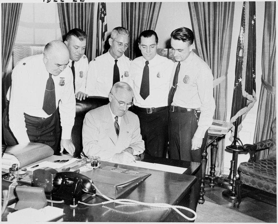 Photograph of President Truman at his desk in the Oval Office, signing H.R. 7695, an act providing a five-day work... - NARA - 200231