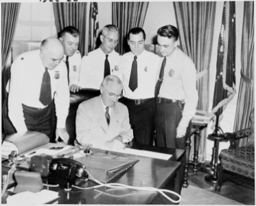 Photograph of President Truman at his desk in the Oval Office, signing H.R. 7695, an act providing a five-day work... - NARA - 200231