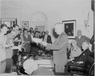 Photograph of President Truman in the Oval Office, reading the announcement of Japan's surrender to assembled... - NARA - 199169 photo