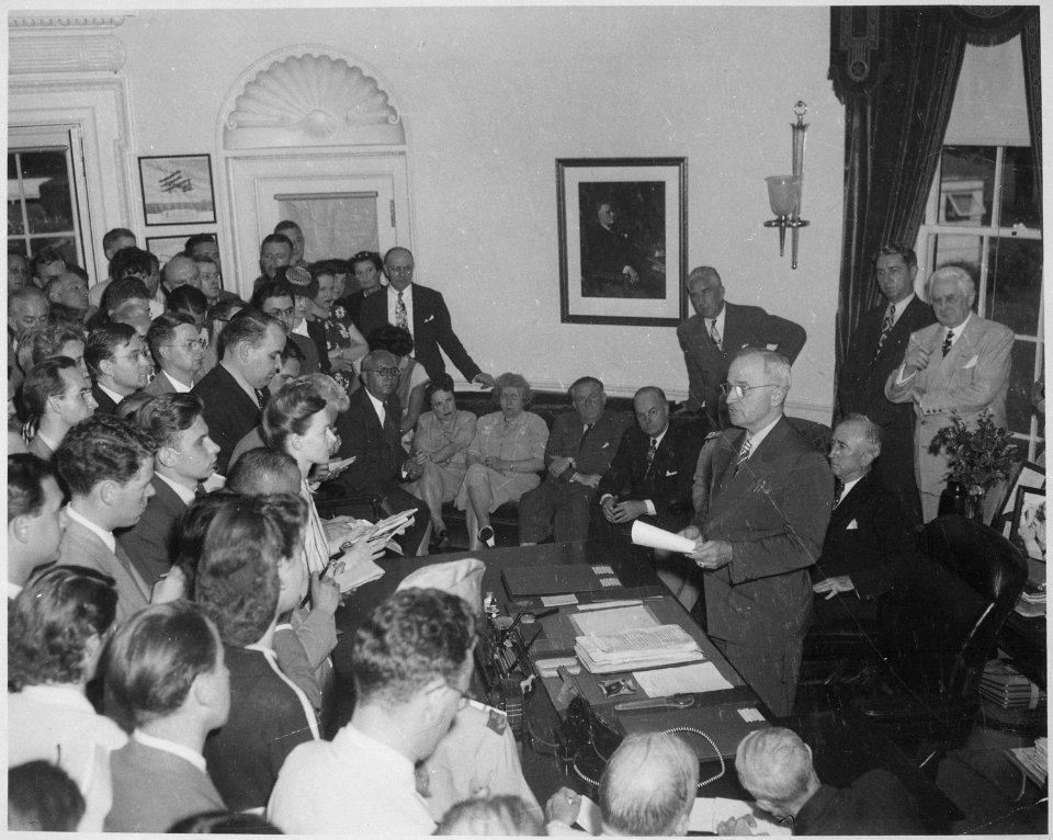 Photograph of President Truman in the Oval Office, reading the announcement of Japan's surrender to assembled... - NARA - 199171