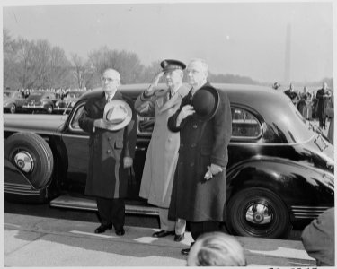 Photograph of President Truman, with two unidentified men, standing beside his car with his hat over his heart... - NARA - 199502