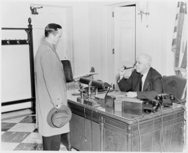 Photograph of William Simmons, receptionist at the White House, seated at his desk talking with an unidentified visitor. - NARA - 199456